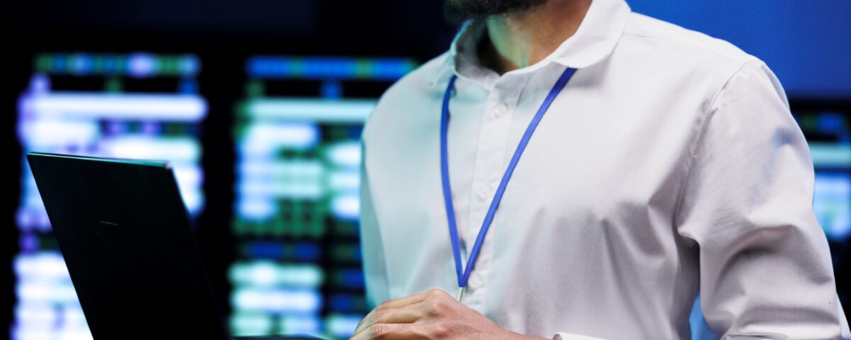Manager using laptop to survey high tech supercomputers providing vast computing resources and storage. Server farm enabling artificial intelligence to process massive datasets for training