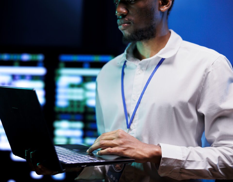 Manager using laptop to survey high tech supercomputers providing vast computing resources and storage. Server farm enabling artificial intelligence to process massive datasets for training